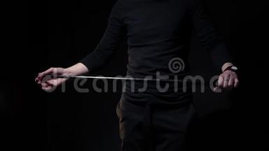 一位身穿黑色运动衫的魔术师展示了一种魔术，手绢是从棍子中出现的，动作缓慢